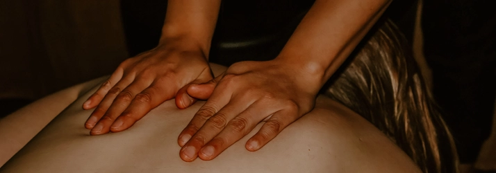 A massage therapist with their hands on a patients upper back.